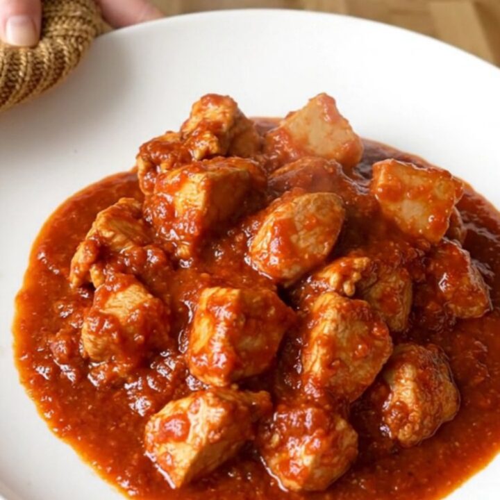 A vibrant bowl of slow-cooked chicken vindaloo with tender potatoes and a rich, spicy red sauce.