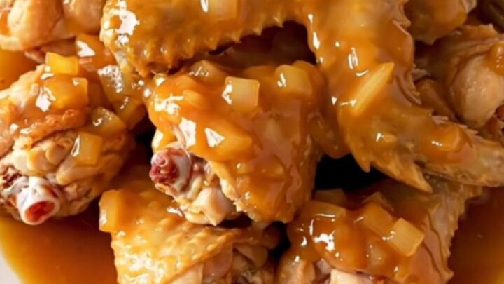 A close-up of slow-cooked chicken wings coated in a thick, glossy orange marmalade barbecue sauce.