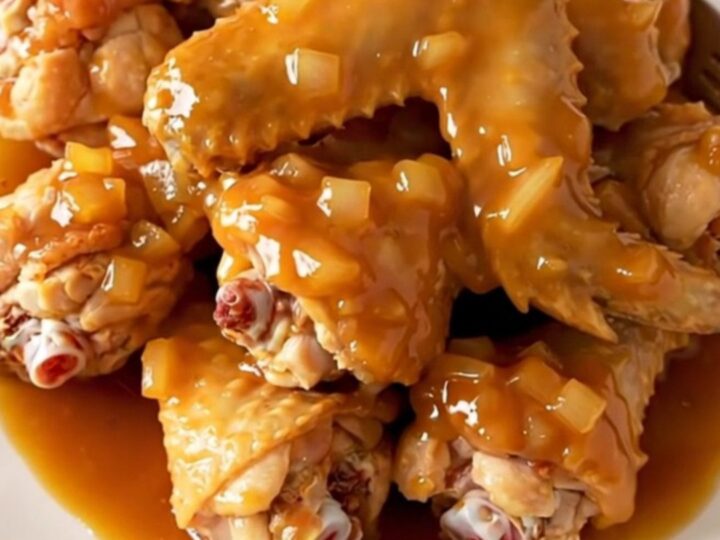 A close-up of slow-cooked chicken wings coated in a thick, glossy orange marmalade barbecue sauce.