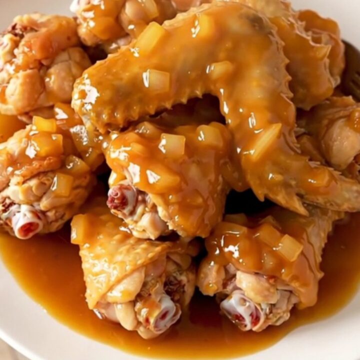A close-up of slow-cooked chicken wings coated in a thick, glossy orange marmalade barbecue sauce.