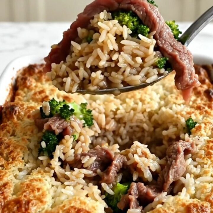 A top-down view of a rectangular ceramic baking dish filled with rice, raw beef strips, and broccoli.