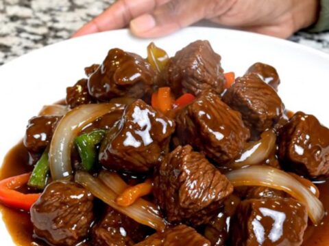 A close-up of tender beef tips and colorful vegetables in a rich hoisin sauce served on a white plate.