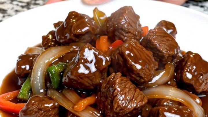 A close-up of tender beef tips and colorful vegetables in a rich hoisin sauce served on a white plate.