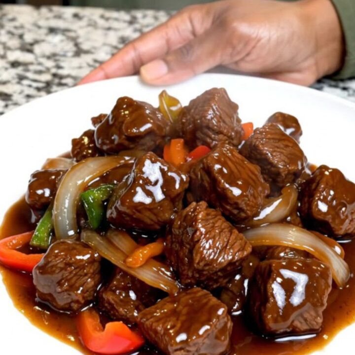 A close-up of tender beef tips and colorful vegetables in a rich hoisin sauce served on a white plate.