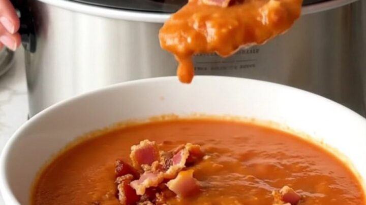 A bowl of creamy tomato soup topped with crispy bacon bits, served in a white shallow bowl.