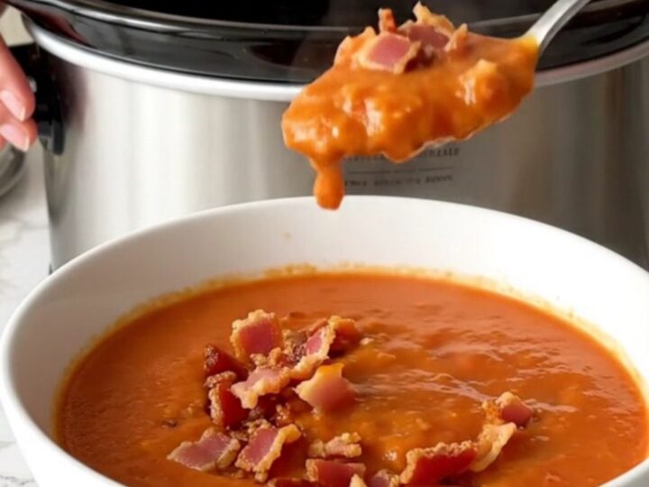 A bowl of creamy tomato soup topped with crispy bacon bits, served in a white shallow bowl.