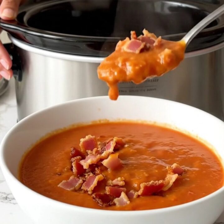 A bowl of creamy tomato soup topped with crispy bacon bits, served in a white shallow bowl.
