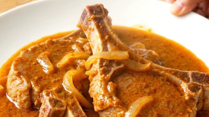 A plate of tender braised pork chops covered in a rich, creamy orange paprika sauce with soft onions.