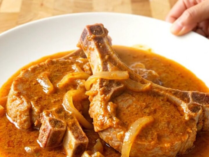 A plate of tender braised pork chops covered in a rich, creamy orange paprika sauce with soft onions.