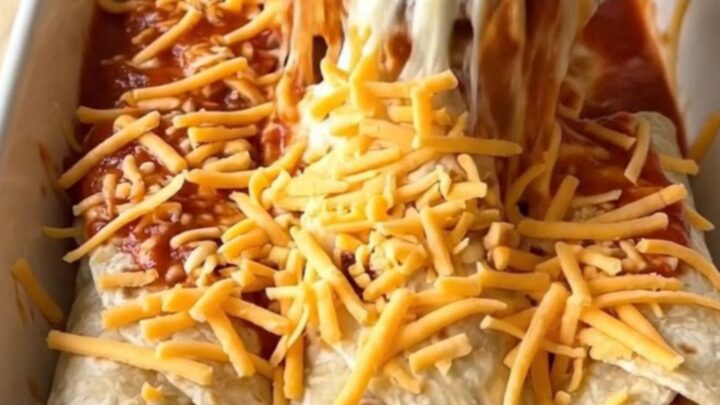 A rectangular ceramic baking dish filled with bean and cheese burritos smothered in red sauce and melted cheddar cheese.