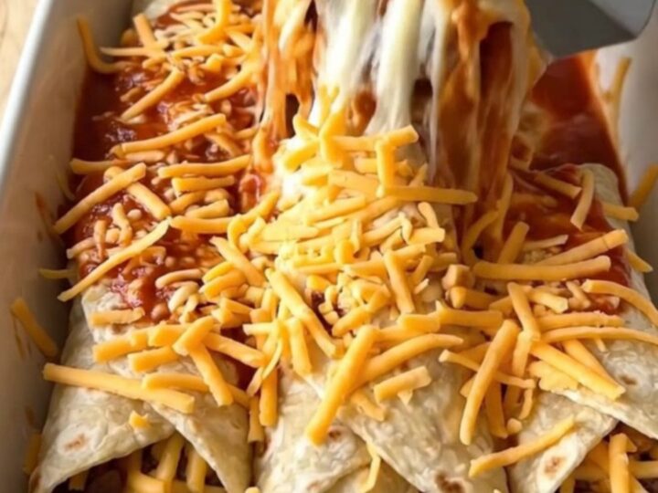 A rectangular ceramic baking dish filled with bean and cheese burritos smothered in red sauce and melted cheddar cheese.