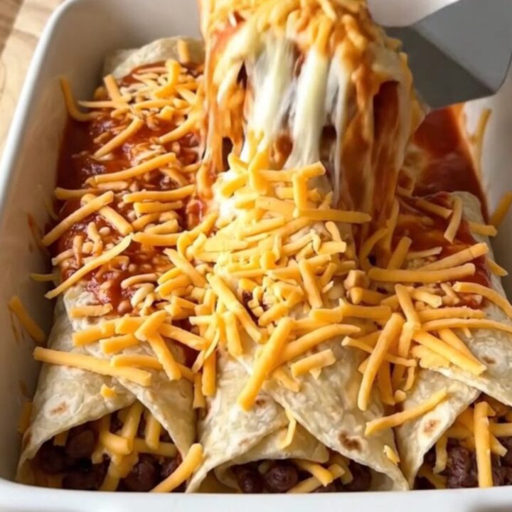 A rectangular ceramic baking dish filled with bean and cheese burritos smothered in red sauce and melted cheddar cheese.