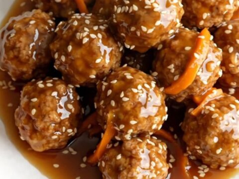 A high-angle shot of frozen turkey meatballs and shredded carrots in a black slow cooker.