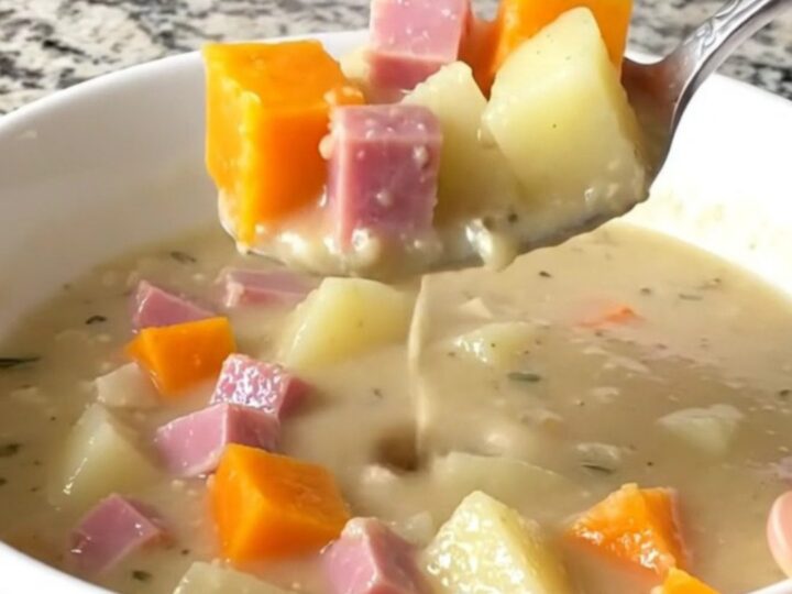 A white shallow bowl filled with creamy slow cooker ham and butternut squash chowder on a granite countertop.