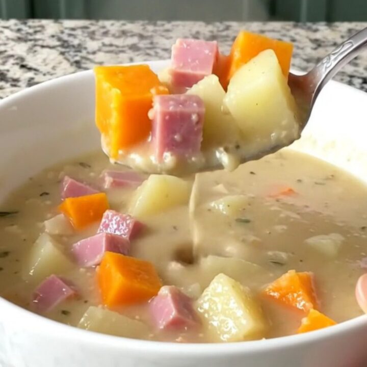 A white shallow bowl filled with creamy slow cooker ham and butternut squash chowder on a granite countertop.