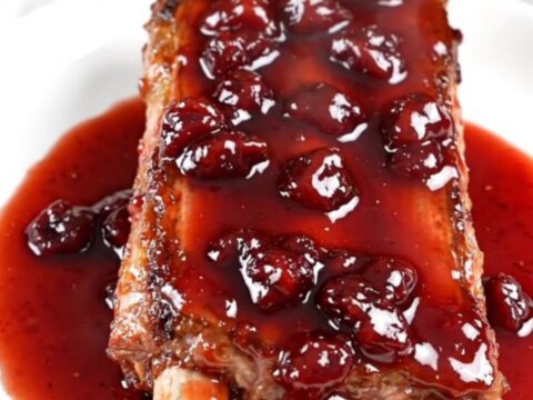 A close-up of slow-cooked baby back ribs with a glossy cherry glaze on a white plate.