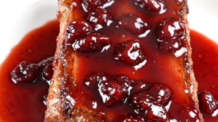 A close-up of slow-cooked baby back ribs with a glossy cherry glaze on a white plate.