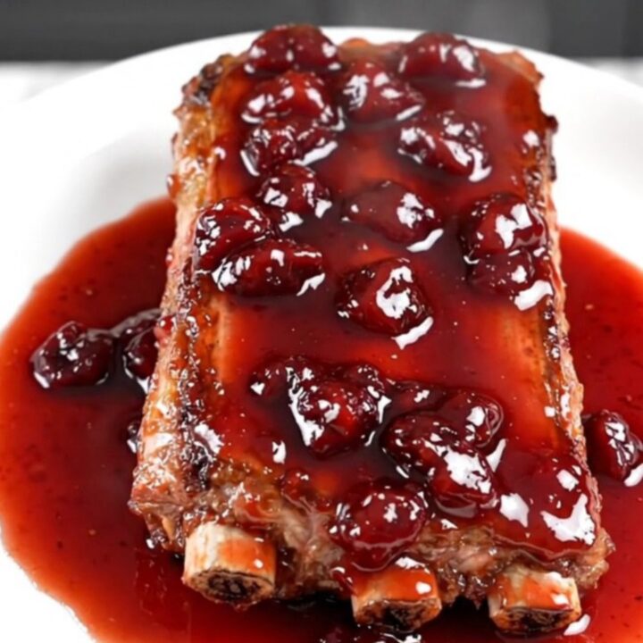 A close-up of slow-cooked baby back ribs with a glossy cherry glaze on a white plate.
