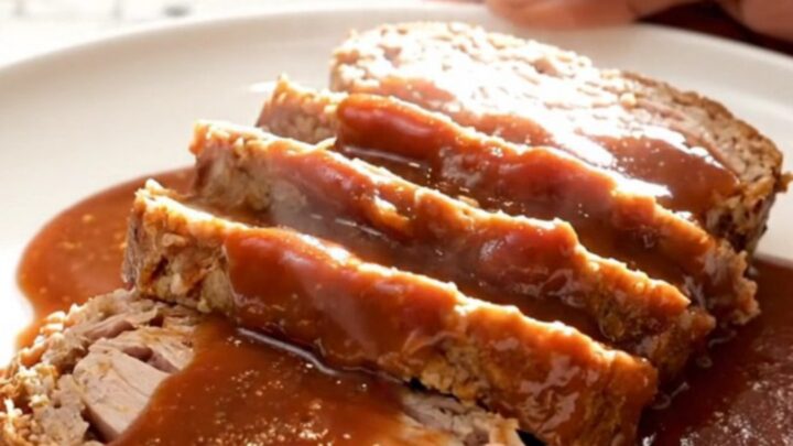 A thick slice of turkey meatloaf covered in a glossy, dark brown sugar and ketchup glaze on a white plate.