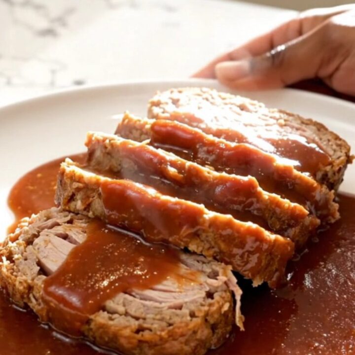 A thick slice of turkey meatloaf covered in a glossy, dark brown sugar and ketchup glaze on a white plate.