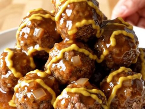 A stainless steel slow cooker filled with maple Dijon glazed meatballs and diced onions on a butcher block counter.