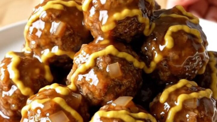 A stainless steel slow cooker filled with maple Dijon glazed meatballs and diced onions on a butcher block counter.