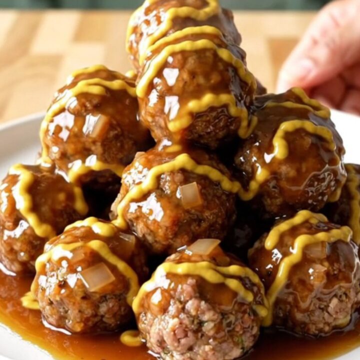 A stainless steel slow cooker filled with maple Dijon glazed meatballs and diced onions on a butcher block counter.