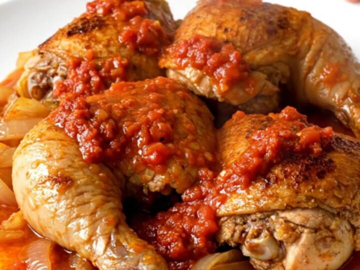 A top-down view of raw chicken thighs, carrots, onions, and harissa sauce in a slow cooker.