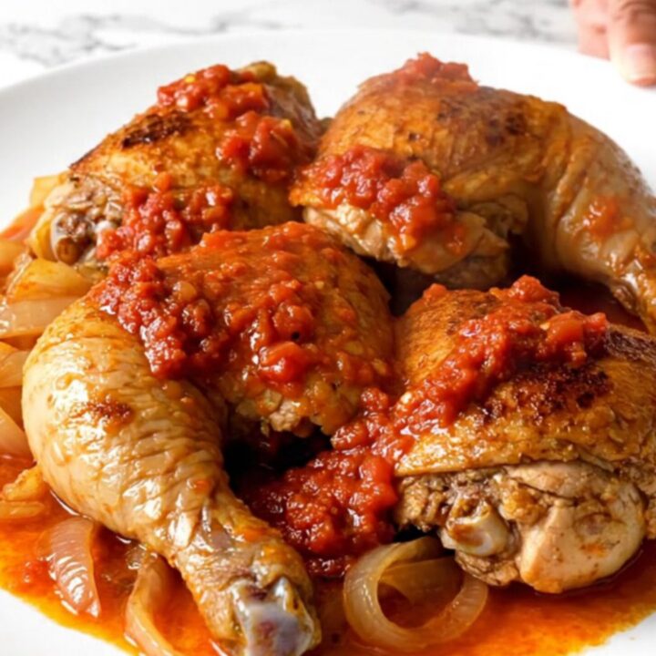 A top-down view of raw chicken thighs, carrots, onions, and harissa sauce in a slow cooker.
