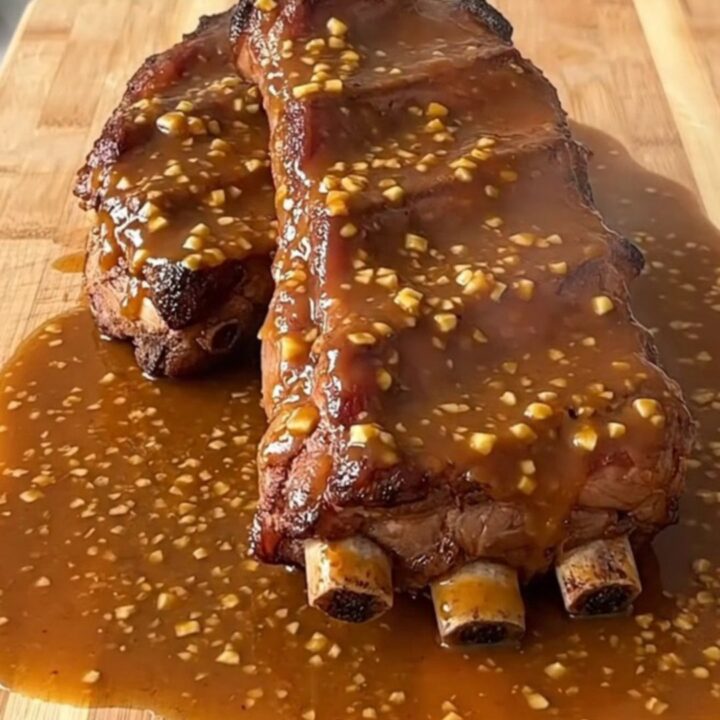 A serving of tender brown sugar garlic country-style ribs served on a wooden board with a glossy sauce.