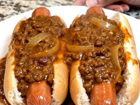 A slow cooker filled with plump hot dogs covered in a thick, hearty chili sauce on a granite countertop.