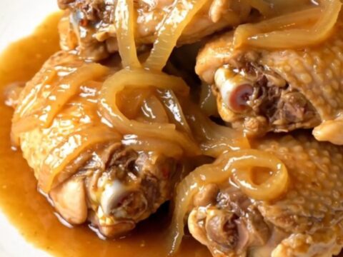 A close-up of tender chicken thighs braised in a glossy ginger sauce in a slow cooker.