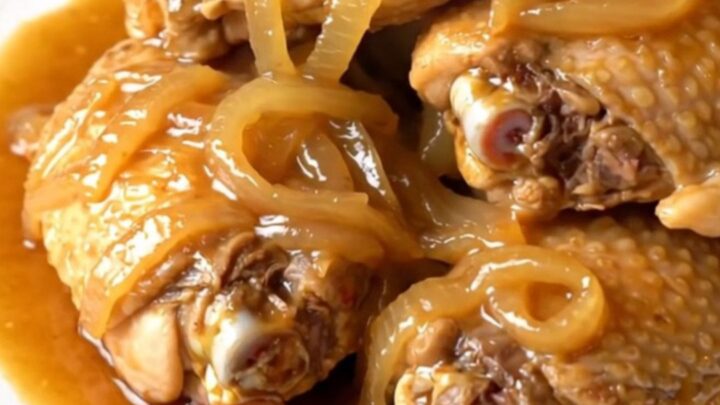 A close-up of tender chicken thighs braised in a glossy ginger sauce in a slow cooker.