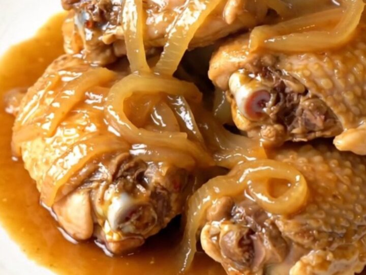 A close-up of tender chicken thighs braised in a glossy ginger sauce in a slow cooker.