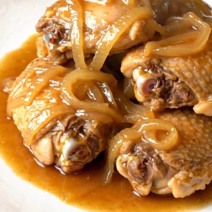 A close-up of tender chicken thighs braised in a glossy ginger sauce in a slow cooker.