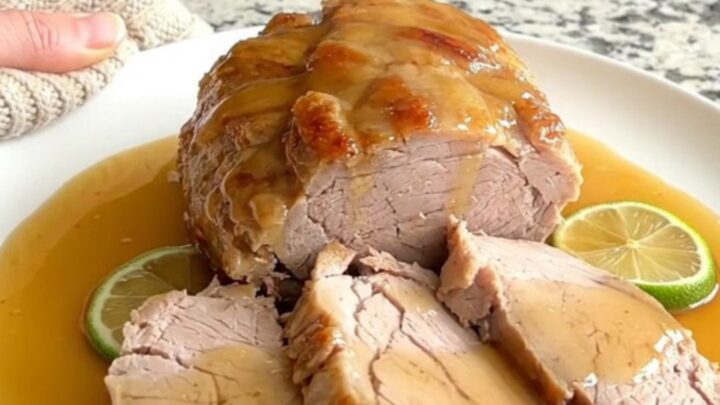A slow cooker filled with honey lime glazed pork tenderloin and fresh lime rounds on a granite countertop.