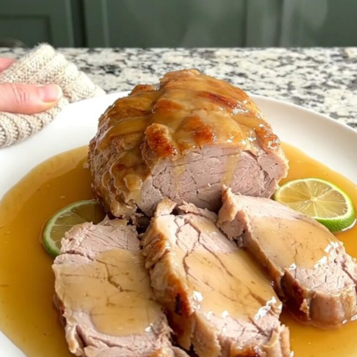 A slow cooker filled with honey lime glazed pork tenderloin and fresh lime rounds on a granite countertop.