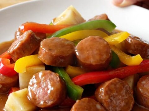 Slow cooker filled with sliced smoked sausage, colorful bell pepper strips, onions, and potato cubes.