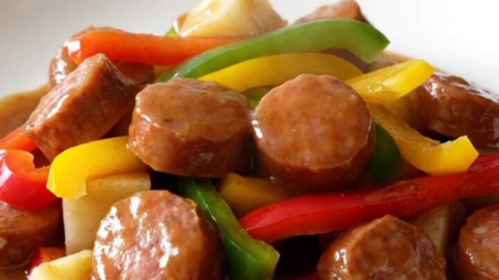 Slow cooker filled with sliced smoked sausage, colorful bell pepper strips, onions, and potato cubes.
