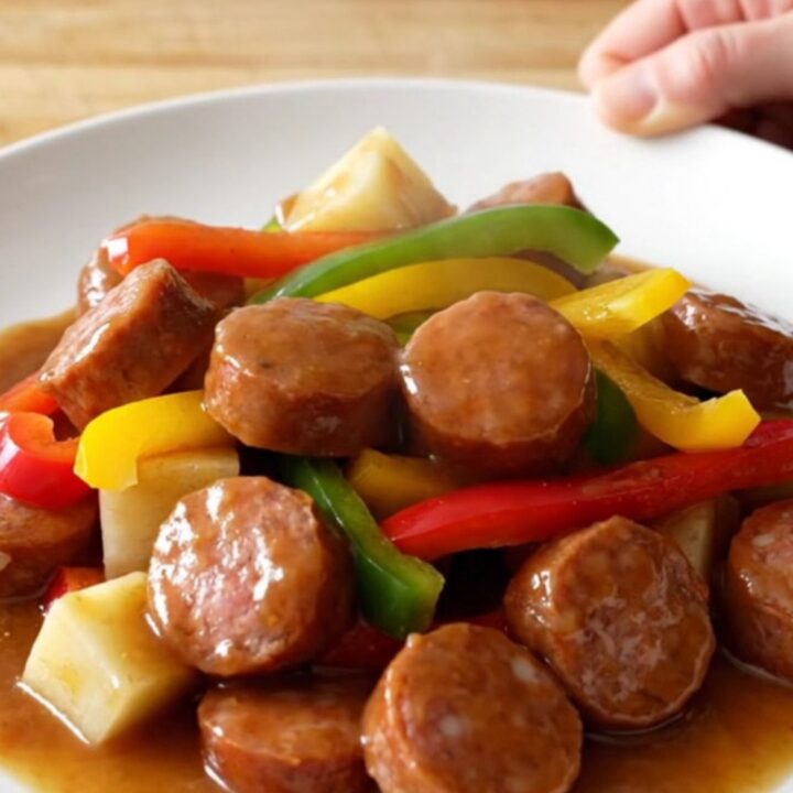 Slow cooker filled with sliced smoked sausage, colorful bell pepper strips, onions, and potato cubes.