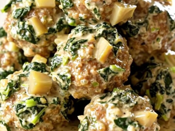 Slow cooker filled with creamy spinach artichoke meatballs on a beige counter.