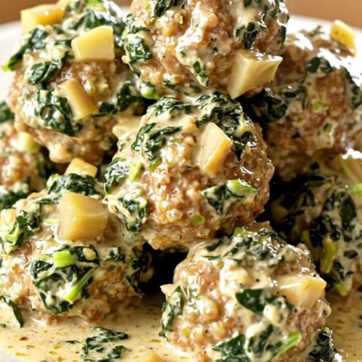 Slow cooker filled with creamy spinach artichoke meatballs on a beige counter.