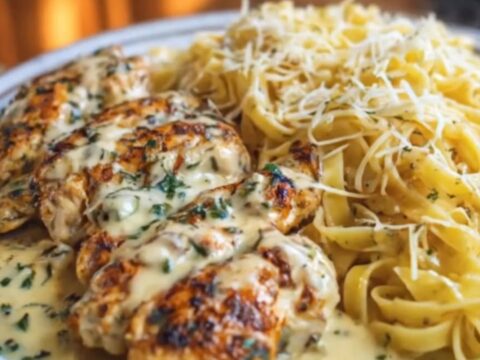 A close-up shot of glossy fettuccine pasta in rich alfredo sauce topped with sliced golden seared chicken.