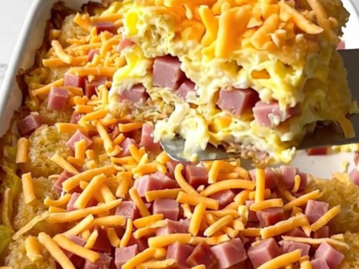 A top-down view of a rectangular ceramic baking dish filled with potato tots, ham, eggs, and melted cheddar cheese.