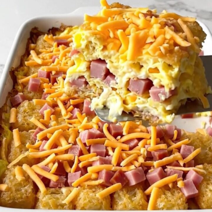 A top-down view of a rectangular ceramic baking dish filled with potato tots, ham, eggs, and melted cheddar cheese.