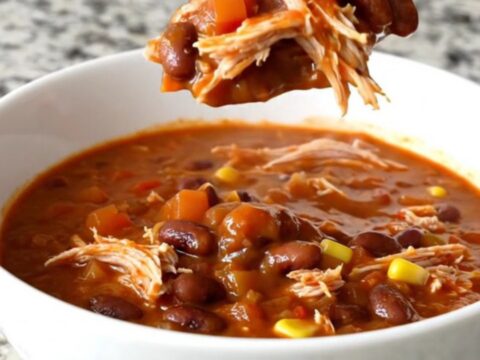A slow cooker filled with shredded turkey chili featuring beans, corn