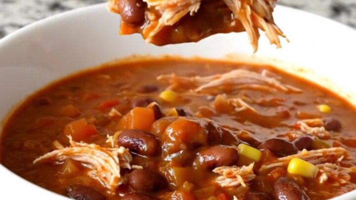 A slow cooker filled with shredded turkey chili featuring beans, corn