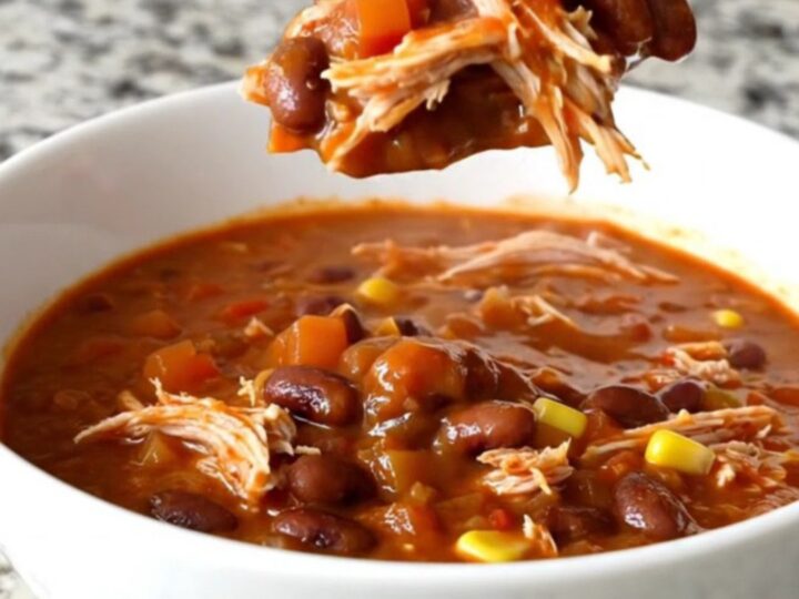 A slow cooker filled with shredded turkey chili featuring beans, corn