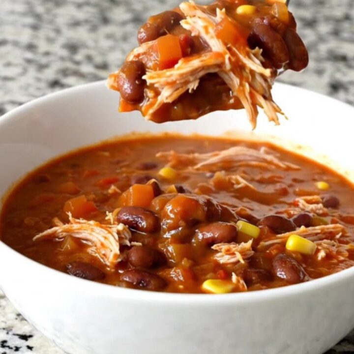 A slow cooker filled with shredded turkey chili featuring beans, corn