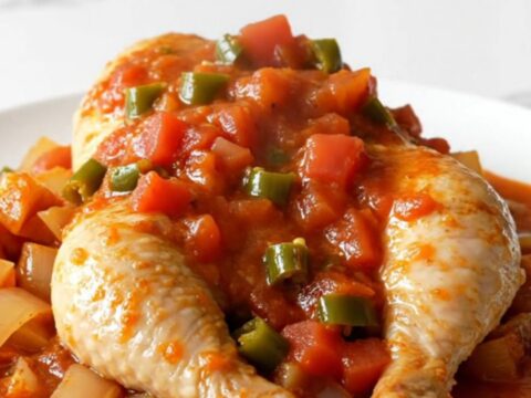 A top-down view of a slow cooker filled with chicken breasts, cubed sweet potatoes, red onion, and a rich tomato sauce.